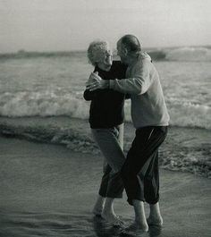 an older couple hugging on the beach by the water