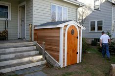 a man standing in front of a small wooden shed on the side of a house