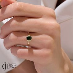 a close up of a person's hand holding a ring with a green stone