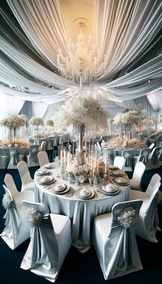 an elegant wedding setup with white flowers and silver cloths on the tables, chandeliers and chairs