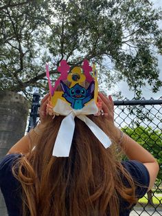 a woman with long hair wearing a paper crown on top of her head in front of a chain link fence