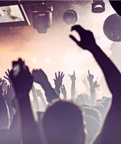 a crowd of people at a concert with their hands up in front of the stage lights