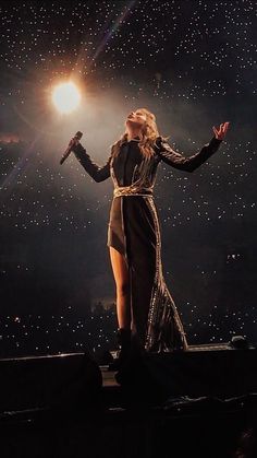 a woman standing on top of a stage in front of a microphone with her arms outstretched