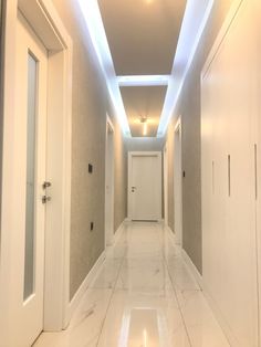 an empty hallway with white walls and flooring is lit by recessed lights above the doors