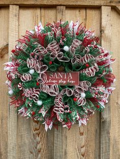 a christmas wreath hanging on the side of a wooden door with santa written on it