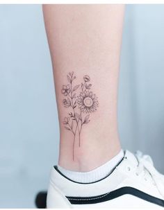 a small sunflower tattoo on the side of a woman's leg, with flowers in it