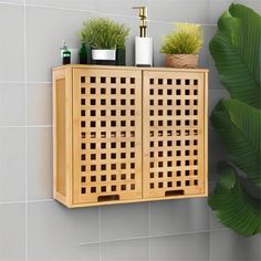 a wooden cabinet with some plants and soaps on the shelf next to it in front of a tiled wall