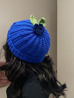 a woman wearing a blue knitted hat with a green leaf on the back of her head