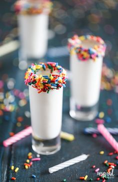 two glasses filled with milk and sprinkles on top of a black table