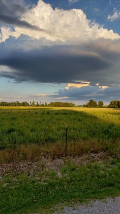 an open field with grass and clouds in the background