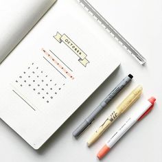 three pens are sitting on top of an open notebook with a calendar in the middle