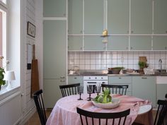 a small kitchen with white cabinets and pink table cloth on the dining room table set for two