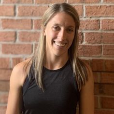 a woman standing in front of a brick wall with her hands on her hips and smiling at the camera