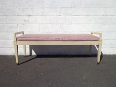 a bench sitting in front of a white brick wall with a pink cushion on it