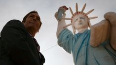 a man standing next to the statue of liberty holding his hands up in the air