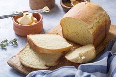 a loaf of bread sitting on top of a wooden cutting board next to bowls of butter