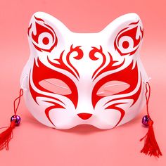 a red and white cat mask with tassels on its ears, against a pink background