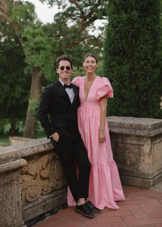 a man and woman in formal wear standing next to each other on a stone wall