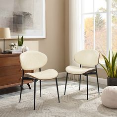 two white chairs sitting next to each other in front of a potted plant on top of a rug