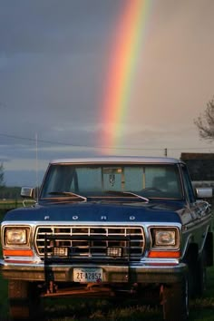 a truck parked in the grass with a rainbow in the sky behind it and a house on the other side