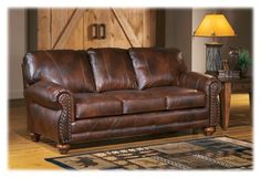 a brown leather couch sitting on top of a wooden floor next to a table and lamp