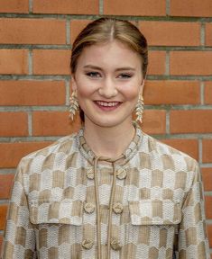 a young woman standing in front of a brick wall smiling at the camera with her hands on her hips