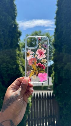 a person holding up a phone case with flowers on the front and back cover, in front of some trees