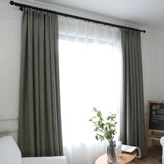 a living room filled with furniture and a large window covered in gray drapes next to a chalkboard