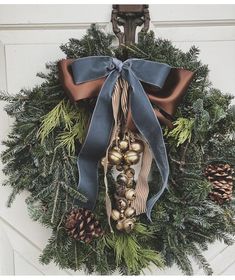 a christmas wreath with bells and pine cones hanging on the front door, decorated with blue ribbon