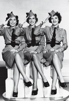 three women in uniforms sitting on top of a white chair with their hands up to their ears