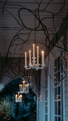 a chandelier with lit candles hanging from it's ceiling in front of windows