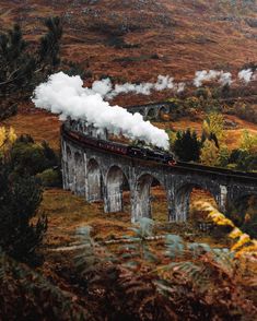 a train traveling over a bridge with steam pouring out of it