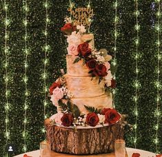 a three tiered cake with red flowers and greenery on the top is surrounded by string lights