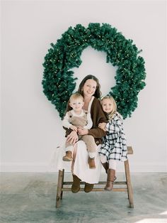 a woman and two children are sitting on a bench in front of a christmas wreath