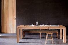 a wooden table with two stools and an open book on it in front of a black wall