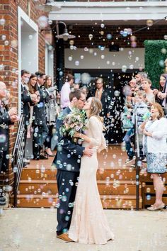 a bride and groom are kissing in front of their wedding party as bubbles fly around them