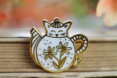 a white and gold cat brooch sitting on top of a wooden table next to flowers