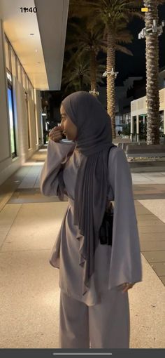 a woman standing in front of a building talking on a cell phone while wearing a hijab