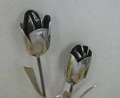 two metal flowers are shown on a white table top with silverware in the shape of tulips