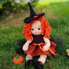 a crocheted doll sitting on the grass wearing a witches hat and orange dress