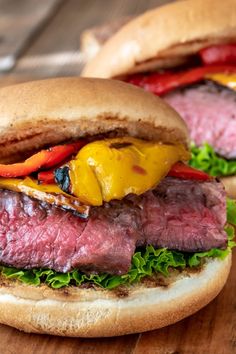 two steak sandwiches with peppers and onions on a wooden table, ready to be eaten