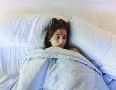 a woman laying in bed under a blanket with her head on top of the pillow