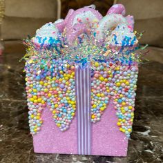 a pink gift box filled with candy and sprinkles on top of a table