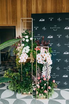 an arrangement of flowers and greenery on display in front of a blackboard sign