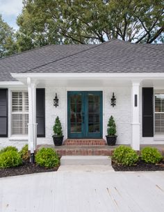 a white brick house with black shutters and green plants on the front porch,