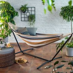 a hammock hanging in front of a white brick wall with potted plants