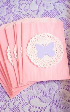 six pink envelopes with lace doily and a butterfly on the front, sitting on a purple tablecloth