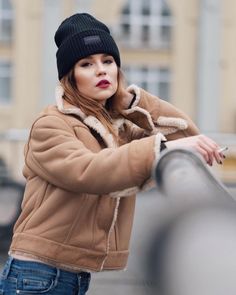 a woman wearing a hat and jacket leaning against a railing with her hand on her hip