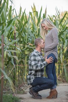 a man kneeling down next to a woman in front of a corn field