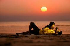 a man and woman laying on the beach at sunset